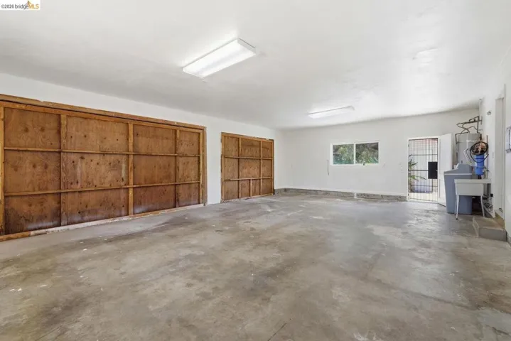 Spacious garage featuring two large wood-paneled doors, concrete flooring, overhead fluorescent lighting, and a utility sink
