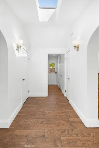 View from secondary double glass entry doors into foyer.  Vaulted ceiling with skylight, arches into thickened walls on both sides and sconce lights.
