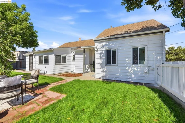 Expansive backyard featuring a manicured lawn, brick patio, mature trees, and a white picket fence