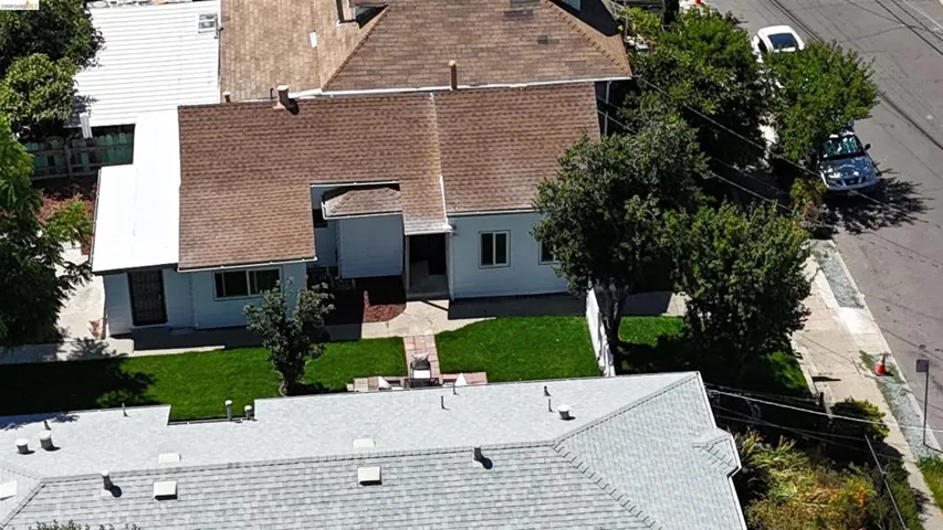 White exterior with a brown shingle roof, featuring a green lawn and mature trees