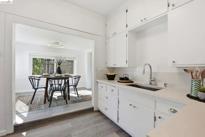 Kitchen featuring white cabinetry with silver hardware, light-toned countertops, and an undermount sink with a gooseneck faucet