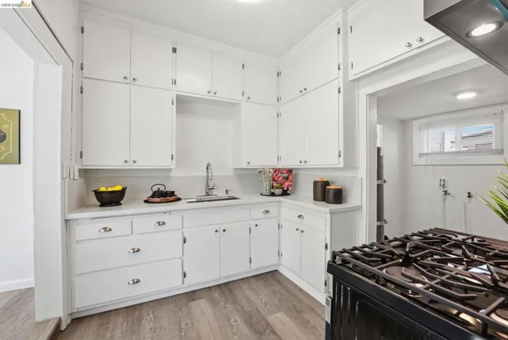 Corner kitchen featuring white cabinetry, a single basin sink with a chrome faucet, light-toned countertops, and wood-finish flooring