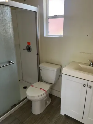 Bathroom featuring a shower with a sliding glass door, a toilet, a single vanity with storage, and wood-finish flooring