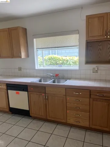 Kitchen featuring a double basin stainless steel sink, wood-finish cabinetry, tile countertops, and a white tile backsplash
