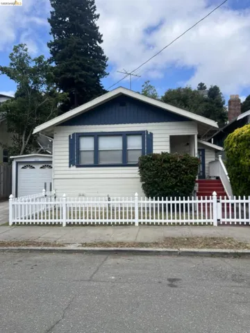 Charming bungalow-style residence featuring a white picket fence, a detached garage with a paneled door, and a prominent front gable with vertical siding
