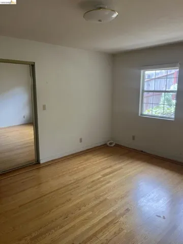 Room featuring wood-finish flooring, a window with natural light, a ceiling-mounted light fixture, and a mirrored sliding closet door