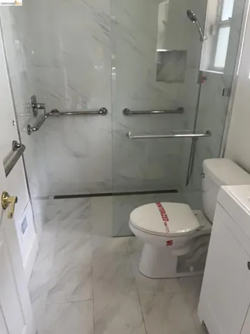 Shower enclosure with glass paneling, white marble-look wall tiling, and chrome grab bars