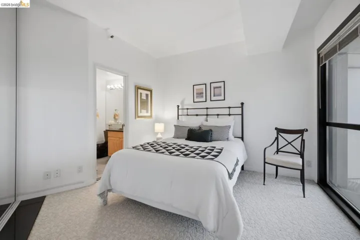 Carpeted bedroom featuring white walls, a large window, and mirrored closet doors