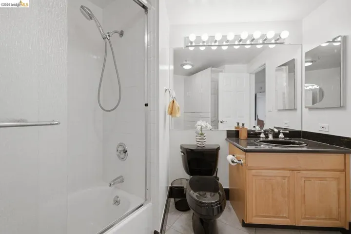 Bathroom featuring a black toilet, wood-finish vanity with dark countertop, large wall-mounted mirror, and a tub-shower combination with sliding glass enclosure