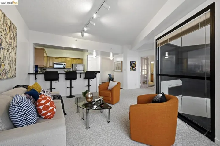Open-concept living area featuring light-colored carpeting, track lighting, and a full-height window with roller​​‌​​​​‌​​‌‌​​‌​​​‌‌​​​‌​​‌‌​​‌‌​​‌‌​​​​ shades