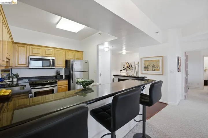 Kitchen featuring light wood cabinetry, stainless steel appliances, dark countertops, and a skylight