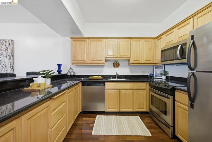 Kitchen featuring light wood cabinetry, dark speckled countertops, and stainless steel appliances including a refrigerator, microwave, and dishwasher
