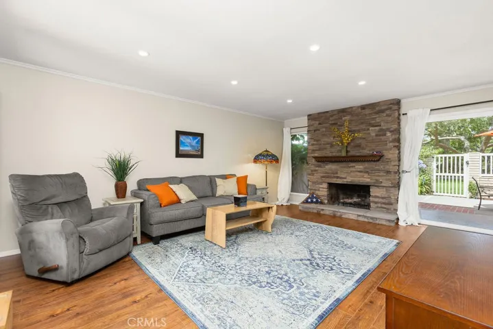 Living room with cozystacked-stone fireplace and easy access to backyard - recessed lighting + laminate wood-tone flooring.
