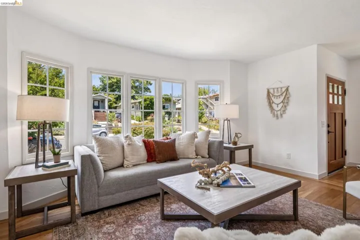 Bright living area featuring a bay window with multiple paneled windows, light wood-finish flooring, white baseboards, and a paneled entry door