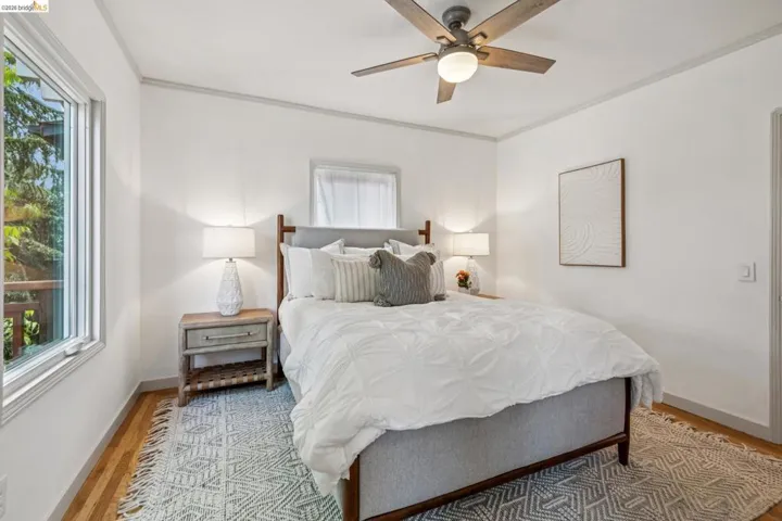 Bright bedroom featuring wood-finish flooring, a ceiling fan with integrated lighting, and a large window