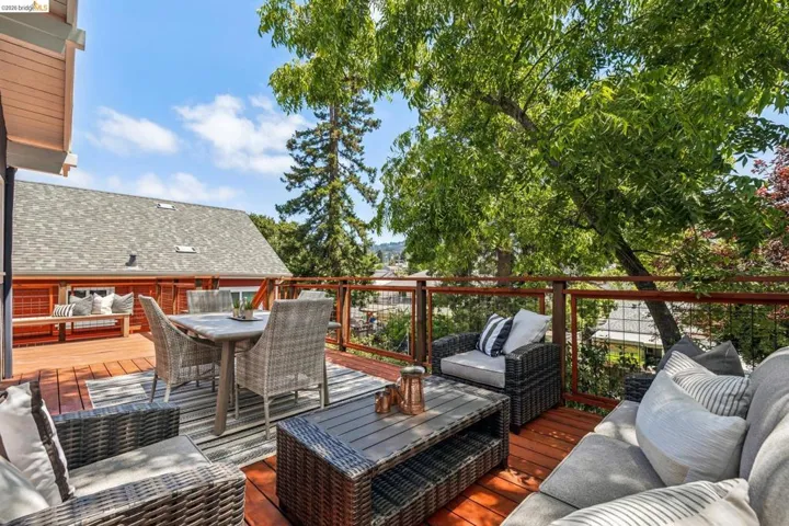 Multi-level wood-decked patio featuring a slatted wood railing with metal infill, mature tree canopy, and ample space for outdoor entertaining