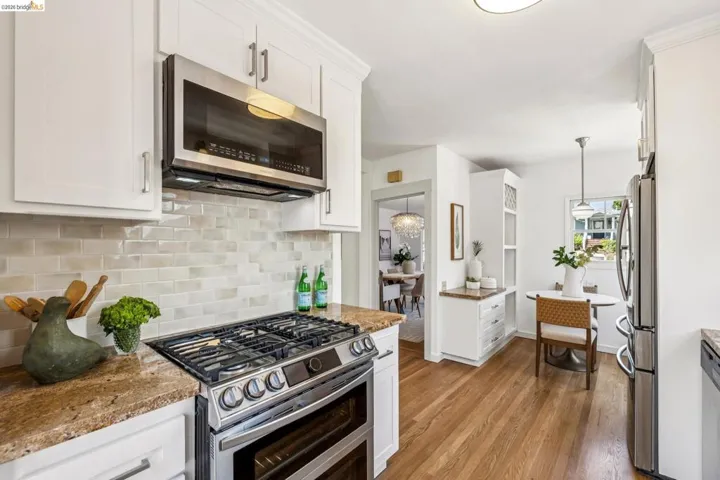 Kitchen featuring stainless steel appliances, granite countertops, white cabinetry, a tiled backsplash, and wood-finish flooring