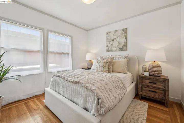 Bedroom featuring wood-finish flooring, two large windows, a built-in overhead light fixture, and crown molding