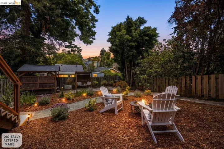 Private backyard featuring a fire pit area, mulched ground cover, landscape lighting, and a shaded outdoor structure