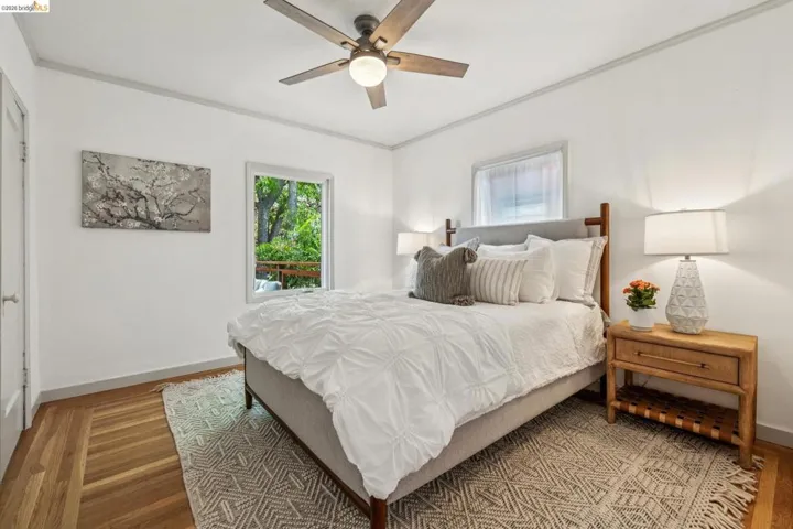 Bedroom featuring hardwood flooring, a ceiling fan with integrated lighting, a window with exterior tree views, and white walls with gray trim