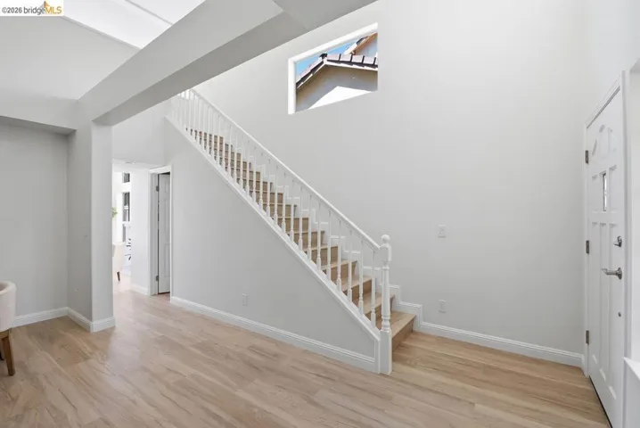 Entryway featuring a staircase with white balusters and wood-finish treads, a transom window, and light wood-finish flooring