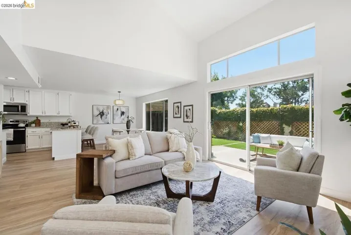 Spacious living area featuring high vaulted ceilings, large transom windows, wood-finish flooring, and a sliding glass door leading to a patio