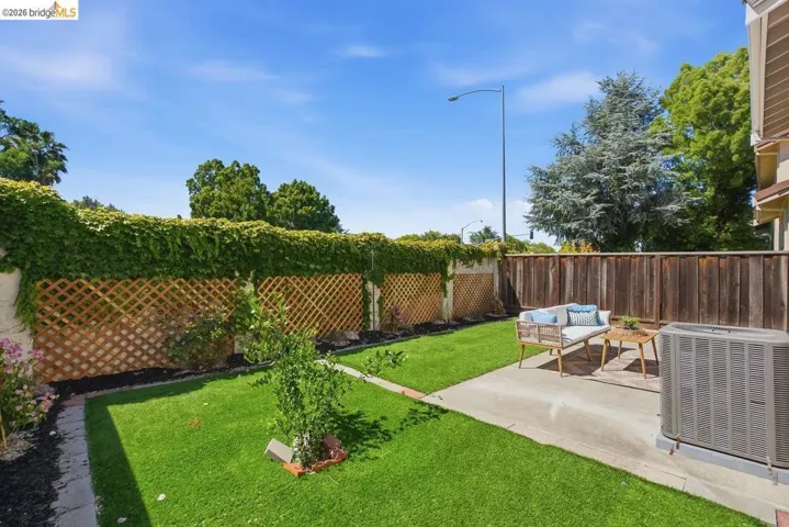 Private backyard featuring a concrete patio, artificial turf, and a wood lattice fence with climbing greenery