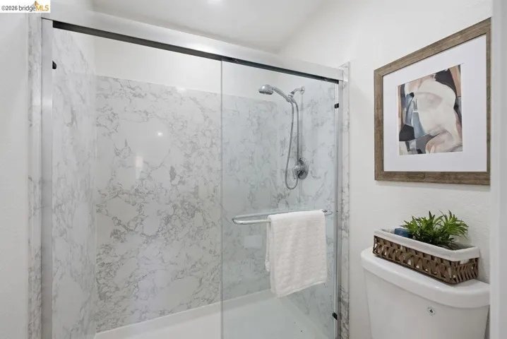 Shower enclosure featuring white marble-look paneling, clear glass sliding doors, and a chrome shower fixture