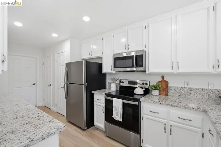 Modern kitchen featuring white cabinetry with brushed nickel hardware, light-toned wood-finish flooring, recessed lighting, and speckled countertops