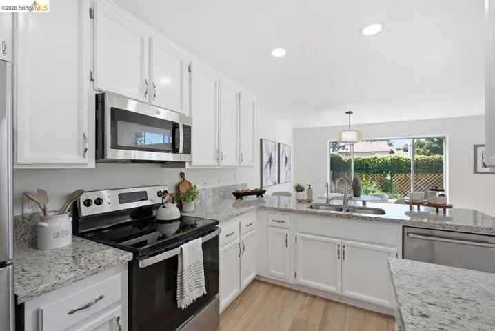 Contemporary kitchen featuring white cabinetry, stainless steel appliances, speckled stone countertops, wood-finish flooring, and recessed lighting