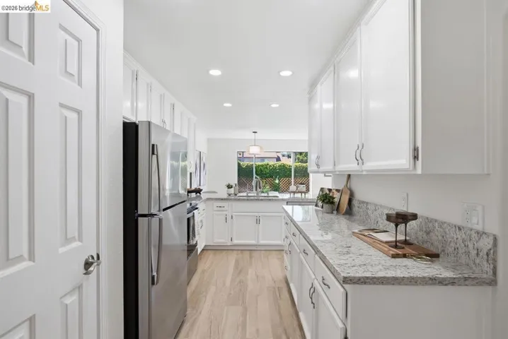 Galley kitchen featuring extensive white cabinetry, stainless steel appliances, speckled countertops, wood-finish flooring, and recessed lighting