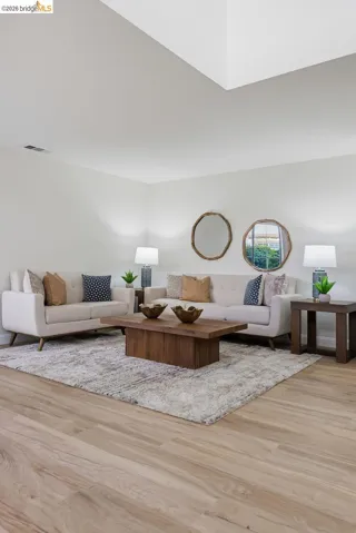 Spacious living area featuring light wood-finish flooring, a recessed ceiling detail, and clean white walls