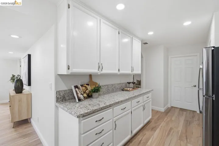 White shaker-style cabinetry with dark hardware, speckled granite countertops, recessed lighting, wood-finish flooring, and a stainless steel refrigerator