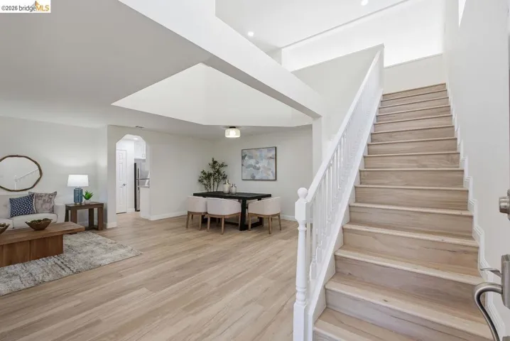 Inviting entryway featuring a light wood-finish staircase with white balusters, wood-finish flooring, recessed lighting, and an open concept living and dining area