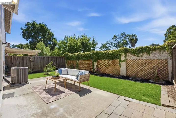 Concrete patio area with artificial turf, bordered by a textured wall featuring lattice panels and climbing foliage