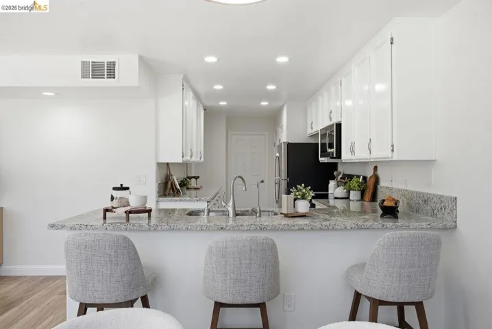 Kitchen featuring a breakfast bar with stone-finish countertops, white cabinetry, a stainless steel sink with a gooseneck faucet, black refrigerator, and built-in microwave