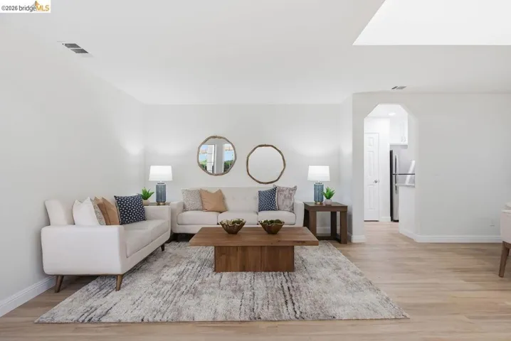 Bright living area featuring light wood-finish flooring, white walls, and an arched entry