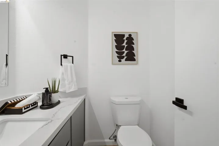 Modern powder room featuring a white vanity with an integrated rectangular sink, a stone-finish countertop, and dark-toned cabinetry
