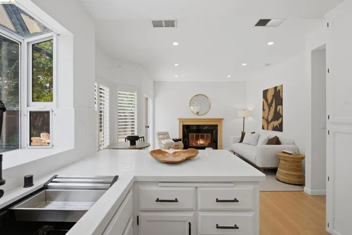 Open-concept living space with white cabinetry, light wood-finish flooring, recessed lighting, and a fireplace with a wood mantle and dark stone surround