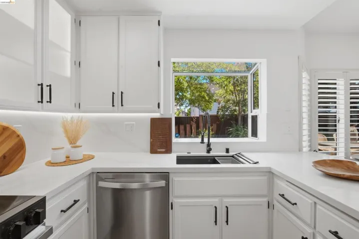 Modern kitchen featuring white cabinetry with matte black hardware, under-cabinet lighting, a stainless steel dishwasher, and a black sink with a pull-down faucet
