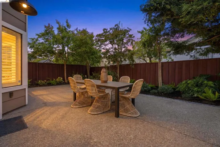 Outdoor patio with an exposed aggregate surface, a wood fence perimeter, and mature trees