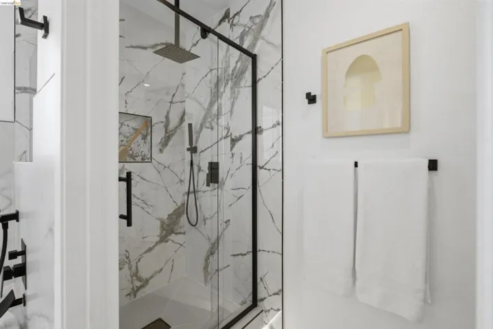 Glass-enclosed shower featuring large format veined wall tiles, a rainfall showerhead, and matte black fixtures