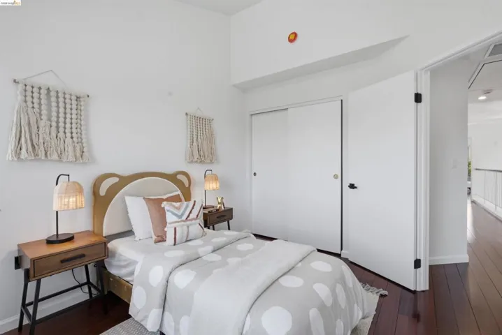 Bedroom featuring rich wood-finish flooring, white walls, a vaulted ceiling, and sliding closet doors