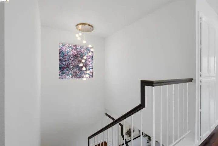 Staircase featuring white walls, a contemporary multi-bulb pendant light fixture, and a dark wood handrail with white balusters