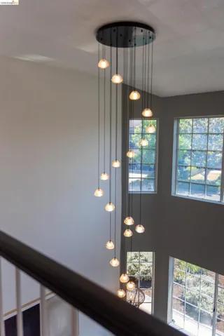 Multi-level chandelier with numerous individual glass pendants, complemented by tall windows and a dark wood-finish handrail