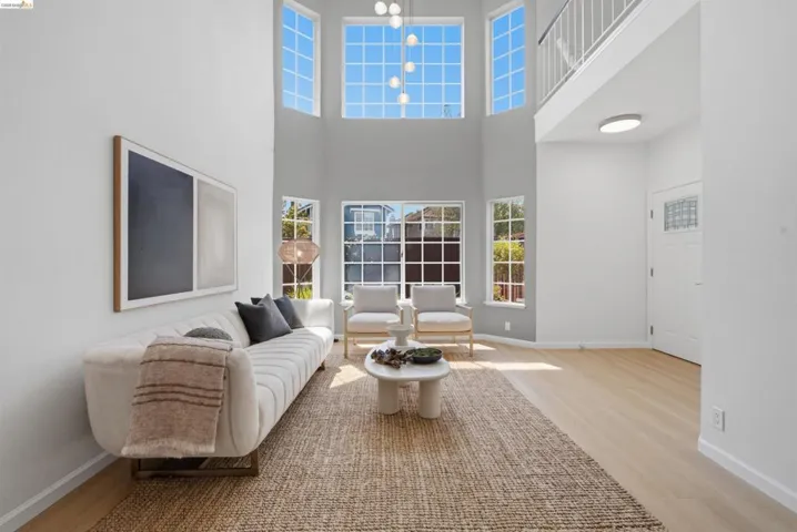 Two-story living area with high ceilings, featuring tall windows and wood-finish flooring