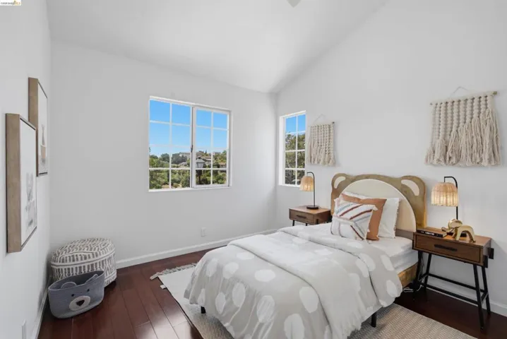 Bright room featuring vaulted ceilings, rich wood-finish flooring, and white walls