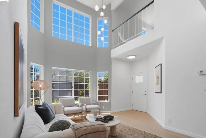 Two-story living area featuring vaulted ceilings, abundant natural light through multiple windows, a second-story interior balcony with white railings, a multi-pendant light fixture, and wood-finish flooring