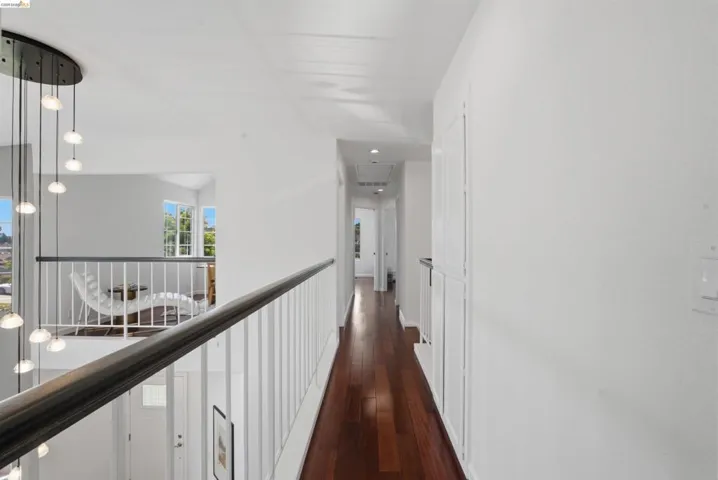 Upper-level hallway featuring wood-finish flooring, white walls, and a contemporary multi-light pendant fixture