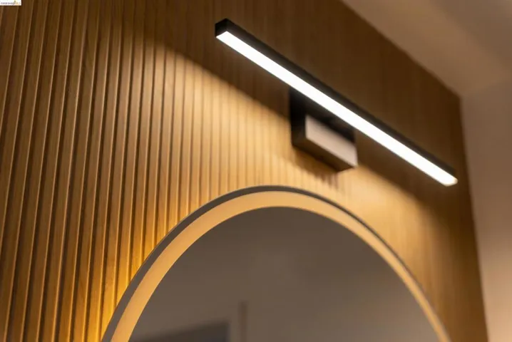 Wood-paneled accent wall featuring a modern linear light fixture and a circular back-lit mirror
